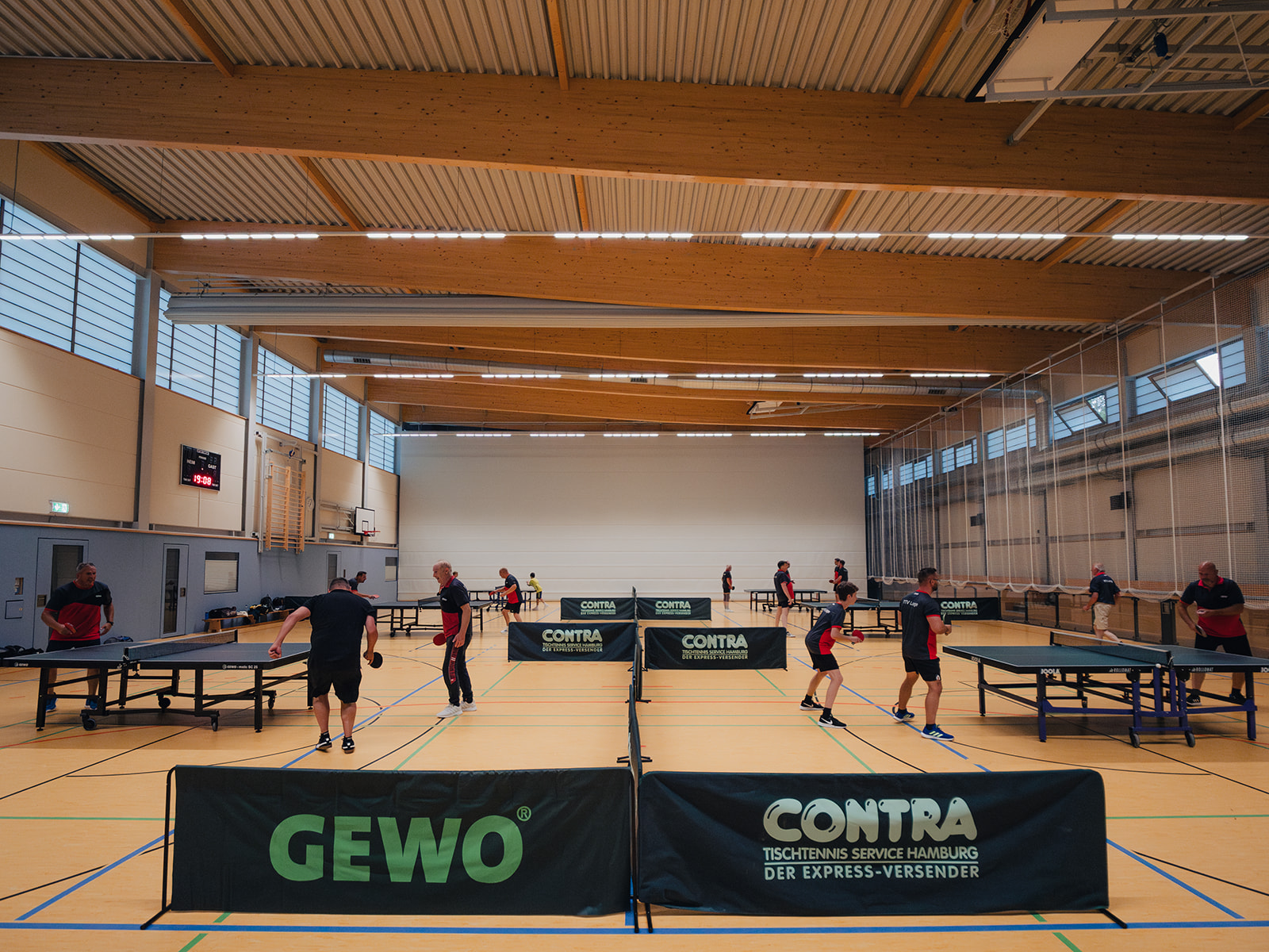 Mehrere Personen spielen in einer Sporthalle an Tischtennisplatten.