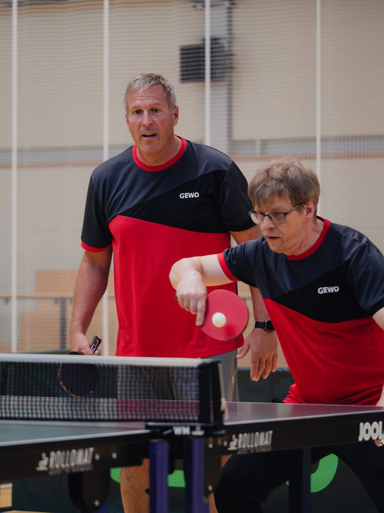 Zwei Männer stehen an der Tischtennisplatte und einer spielt den Ball.