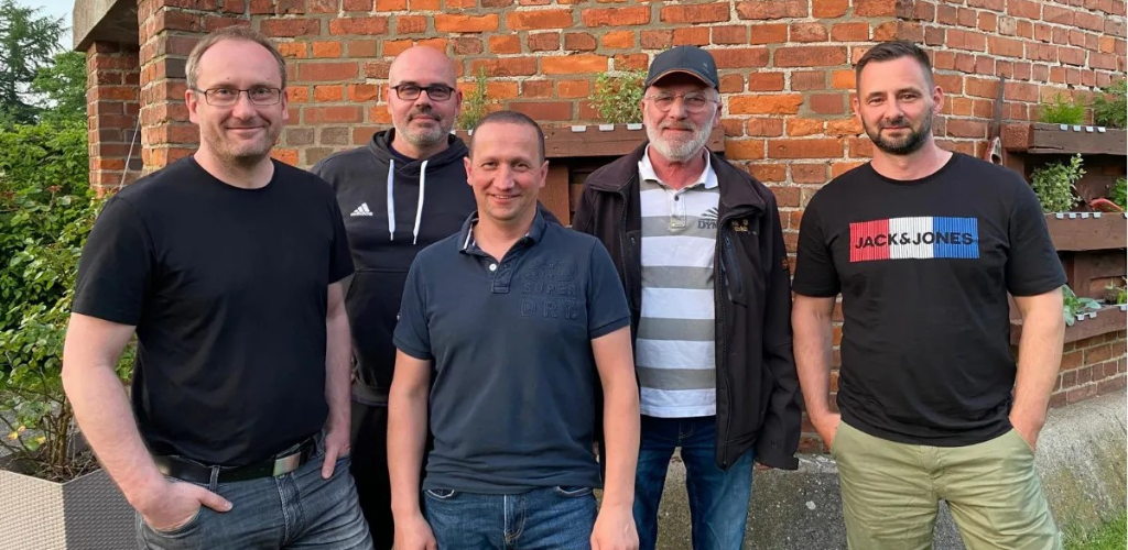 Fünf Männer stehen als Gruppe vor einem Backsteingebäude.