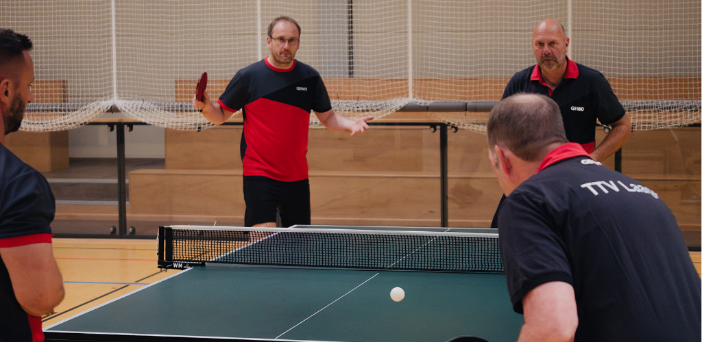 Vier Männer spielen zusammen an einer Tischtennisplatte.