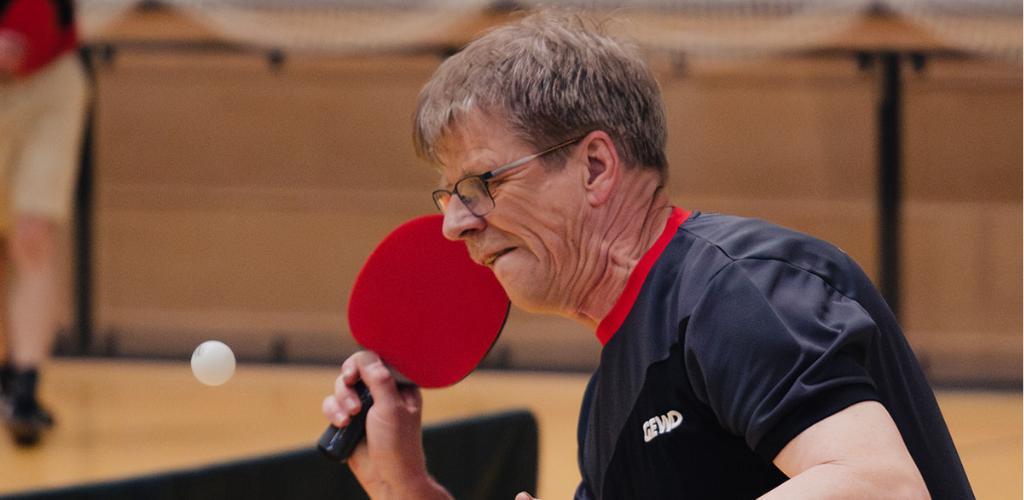 Ein Mann hält einen Tischtennisschläger in der Hand und spielt einen Ball.